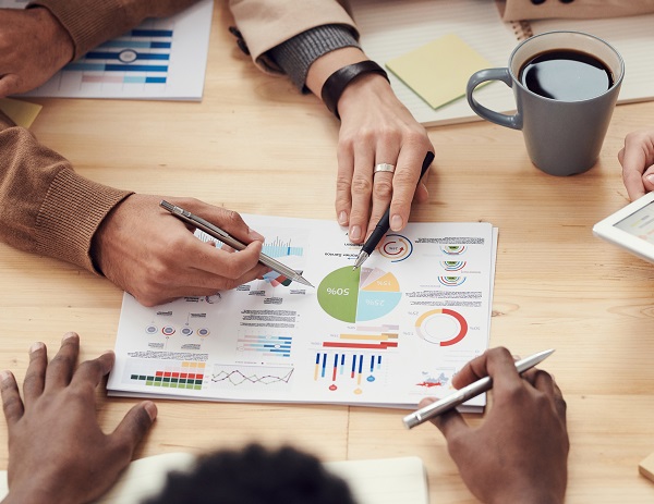 multiple hands pointing to financial graphs on the table